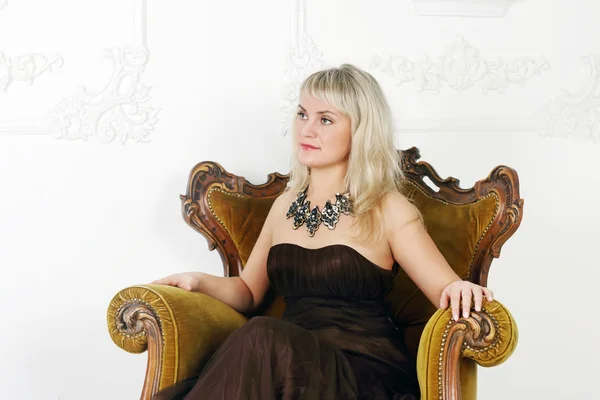 Young woman in brown dress sits in vintage chair and looks away — Stock Photo, Image