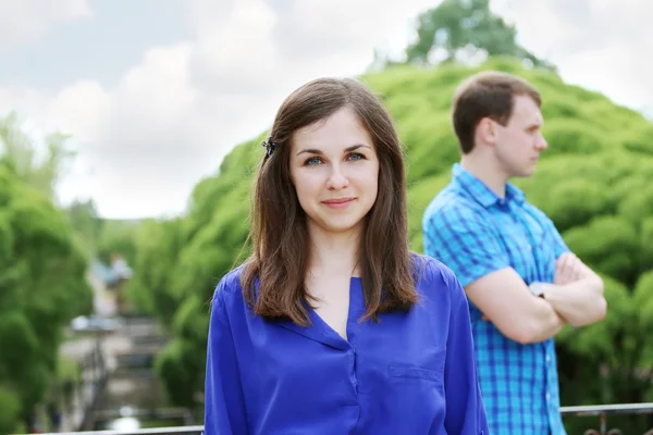 Sorrindo jovem mulher em azul no parque de verão e homem fica atrás — Fotografia de Stock
