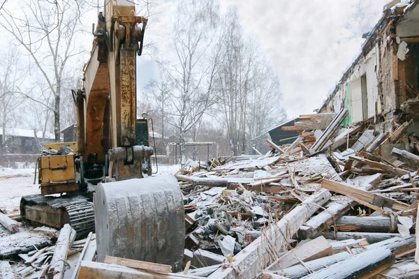 Scavatore demolizione tronco casa in legno in nevicata il giorno d'inverno Immagine Stock