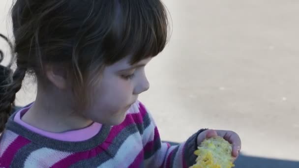 Pequeña linda chica come maíz hervido en mazorca al aire libre en verano — Vídeos de Stock