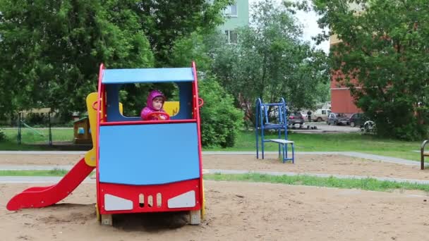 작은 행복한 소녀는 흐린 날에 놀이터에서 색깔의 나무 차에 앉아 — 비디오