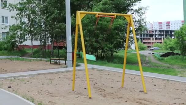 Swinging swing at playground near residential building at cloudy day — Stock Video