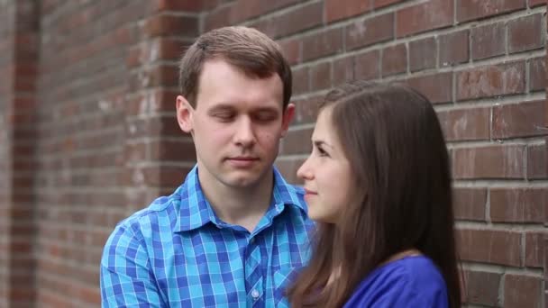 Чоловік і жінка дивляться один на одного і цілуються біля цегляної стіни в літній день — стокове відео
