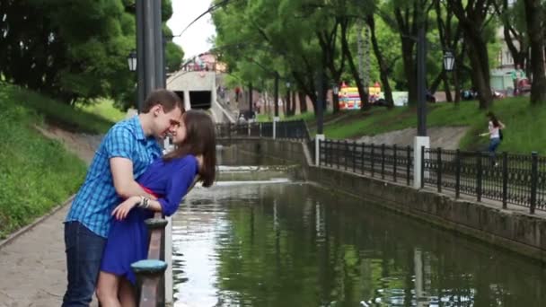 Мужчина наклоняется над женщиной и целует ее возле маленькой реки в парке в летний день — стоковое видео
