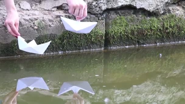 Ruce muže a ženy zahájení papírové lodě na vodu v parku v letní den — Stock video