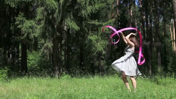 Young woman in dress dances with pink ribbon in summer forest