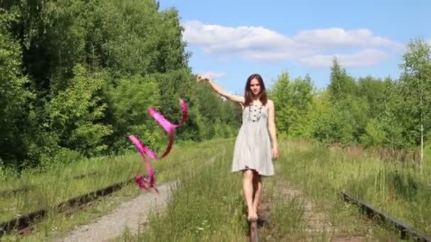 Schönes Mädchen mit Schleife geht an Sommertagen auf alte Schiene im Wald — Stockvideo