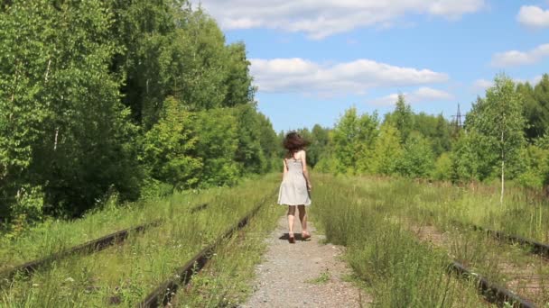 Jolie fille souriante en robe marche sur le chemin de fer à la journée ensoleillée 