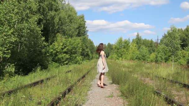 Красивая улыбающаяся девушка в платье танцует на железной дороге в солнечный день — стоковое видео