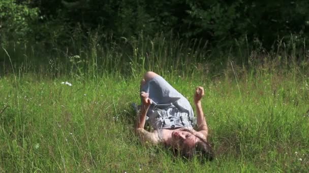 Beautiful girl lies on grass, flips and looks at camera at summer day — Stock Video