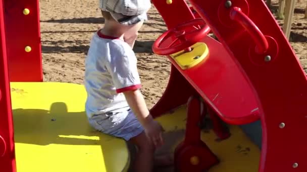 Happy little handsome boy monta em carro de brinquedo de madeira no parque infantil — Vídeo de Stock