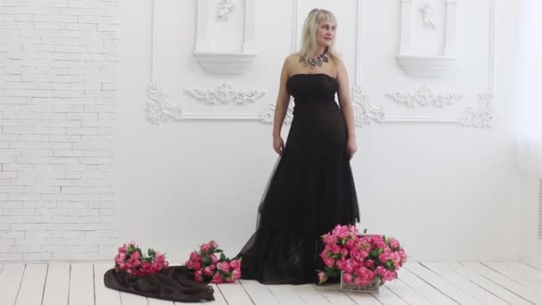 Young woman in long dress poses in white studio with flowers — Stock Video