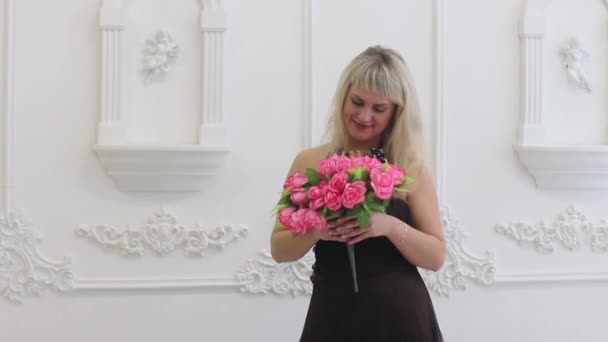 Jovem mulher em vestido marrom detém flores cor-de-rosa e cheira no estúdio branco — Vídeo de Stock