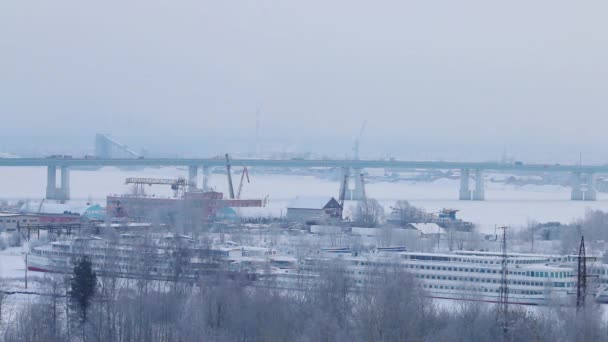 Bilar går på vägen överbryggar över frusna floden med fartyg i snön på vintern mulen dag — Stockvideo