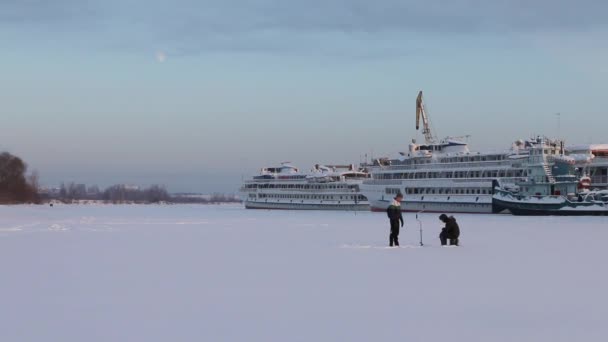 Twee vissers vangen vis op bevroren rivier in de buurt van toeristische schip bij winterdag — Stockvideo