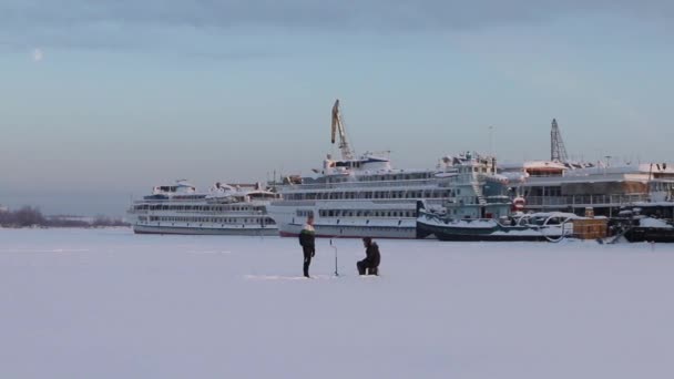 Dois pescadores pegam peixe no rio congelado perto de grande navio turístico no dia de inverno — Vídeo de Stock