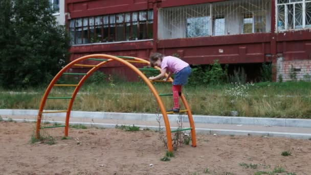 Маленькая девочка забирается на полукруглую лестницу на игровую площадку — стоковое видео