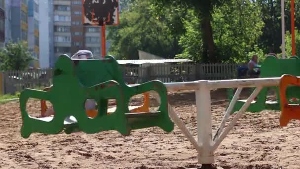 Kleiner süßer Junge mit Brille fährt auf Karussell auf Spielplatz — Stockvideo