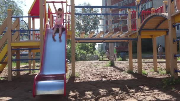 Little pretty girl in pink rolls down slide at playground at sunny day — Stock Video