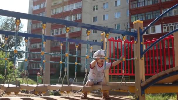 Kis aranyos fiú szemüveges mászik a játszótéren a napsütéses nap — Stock videók