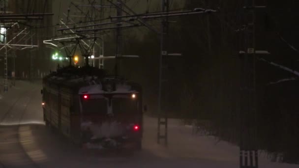 Kleiner Personenzug fährt bei Schneefall in der Winternacht unter Brücke durch — Stockvideo