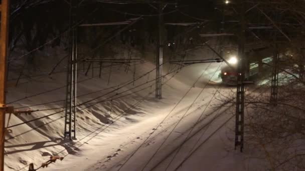 Пасажирський поїзд їде залізницею під мостом взимку вночі під час снігопадів — стокове відео