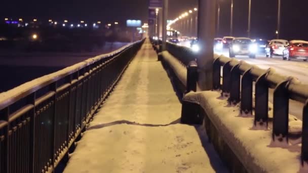 Много машин движется по мосту в зимнюю ночь во время снегопада — стоковое видео
