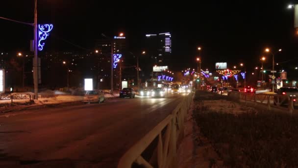 Автомобили, идущие по улице с освещением в темную зимнюю ночь в городе — стоковое видео