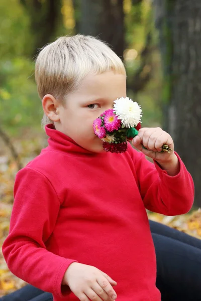 Pequeño chico rubio en rojo huele flores — Foto de Stock