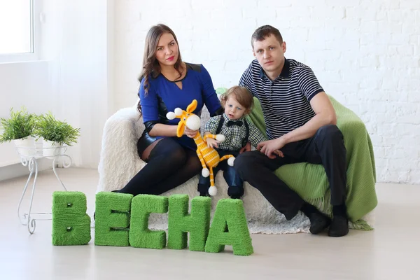 Famiglia di tre persone seduta sul divano bianco in camera con testo verde su fl — Foto Stock