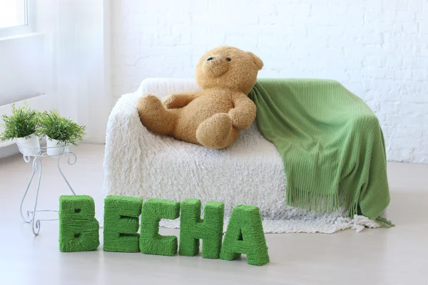 Room with white couch, toy bear and green text on floor: Spring — Stock Photo, Image