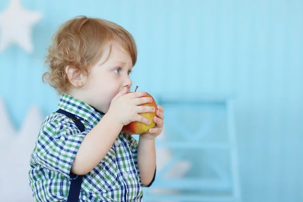 Kleiner süßer Junge mit lockigem Haar beißt roten Apfel und träumt — Stockfoto