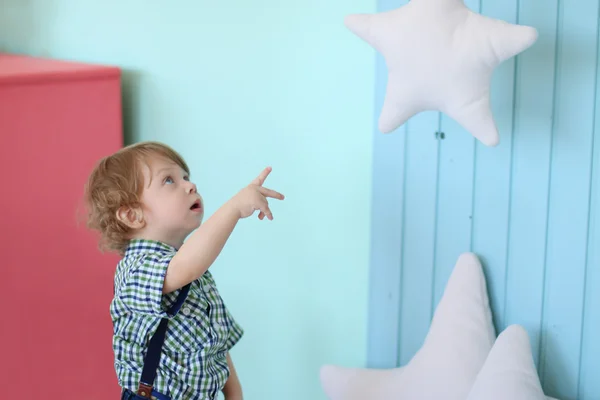 Little handsome curly boy looks and points at soft hanging star — Stock Photo, Image