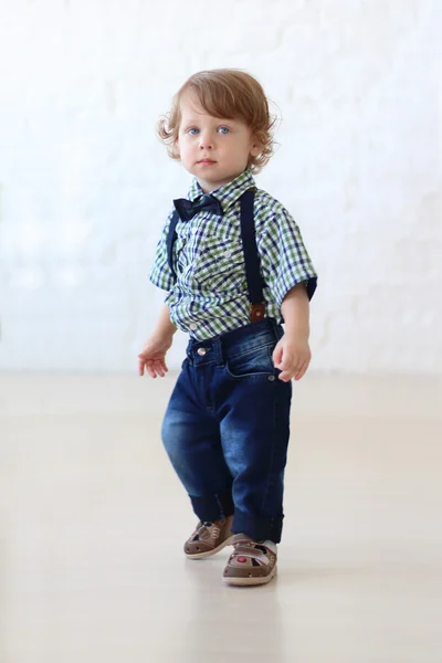 Pequeño guapo rizado chico en jeans stands en habitación — Foto de Stock