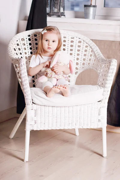Aranyos szőke kislány puha játék ül a nagy fonott szék — Stock Fotó