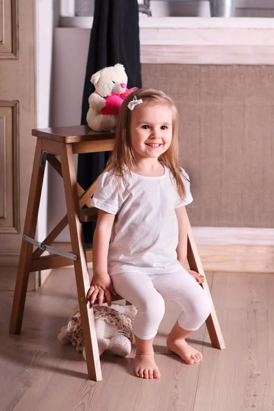 Piccola ragazza bionda carina seduta su una piccola scala di legno in camera wi — Foto Stock