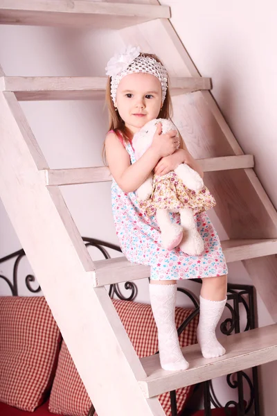 Little cute blond girl in dress sitting on wooden stairs with so — Stock Photo, Image