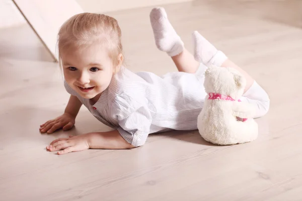 Klein schattig blond meisje in striped shirt is glimlachend op verdieping met — Stockfoto