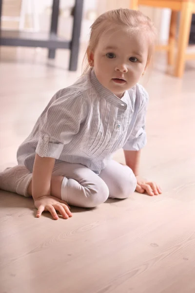 Little cute blond girl in striped shirt sitting on wooden floor — Stock Photo, Image