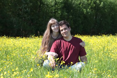 Mutlu kadın ve adam yaz çayır, sarı çiçekler arasında oturmak