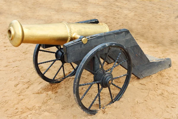 Oude gele metaal kanon met zwarte wielen op zand buiten — Stockfoto