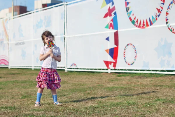 快乐的小女孩，穿着短裙的舔棒棒糖在草地上 — 图库照片