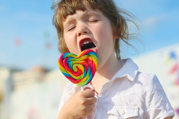 Feliz niña lame piruleta brillante al aire libre en la ciudad —  Fotos de Stock