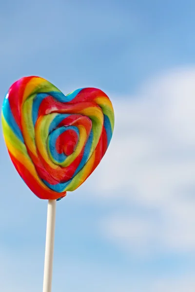 Sweet rainbow lollipop on stick and blue sky at summer sunny day — Stock Photo, Image