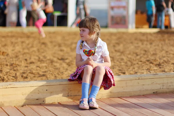 Feliz niña se sienta con piruleta brillante y mira hacia otro lado — Foto de Stock