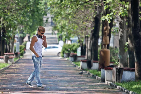 Hombre con gafas de sol camina por callejón con árboles verdes y bancos —  Fotos de Stock