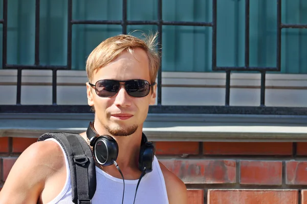 Pohledný mladý muž v sluneční brýle a sluchátka představuje na ulici — Stock fotografie