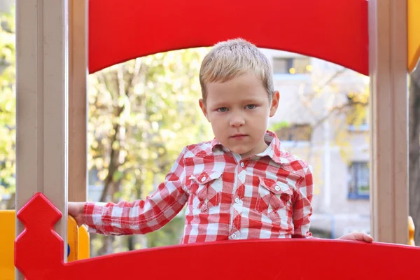 Menino bonito na camisa fica no playground no dia de outono — Fotografia de Stock