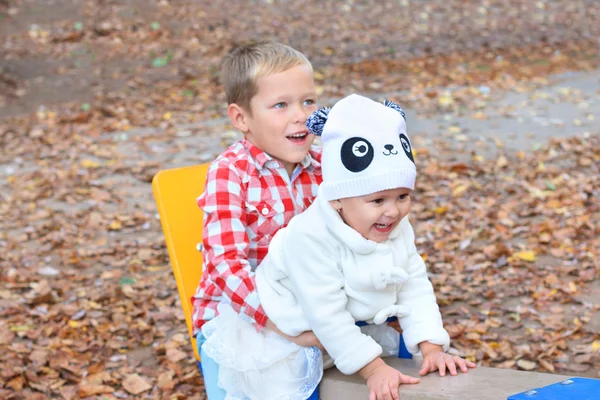 Happy beautiful brother and sister play on seesaw at autumn day. — Stock Photo, Image