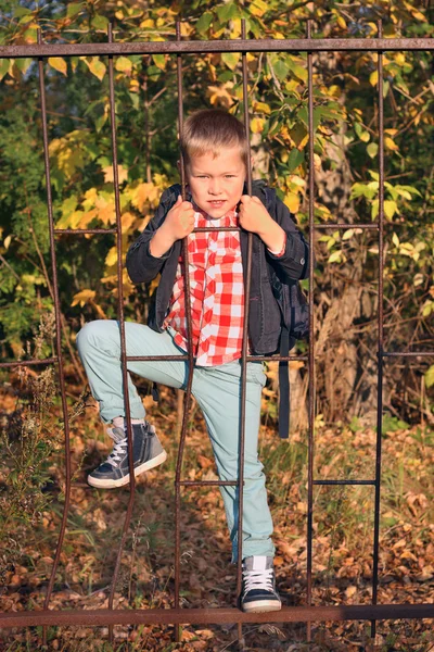 Menino bonito em jeans sobe na cerca de treliça de ferro — Fotografia de Stock